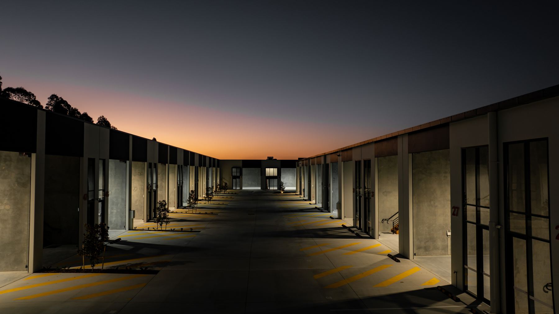 A completed business park at dusk, a row of units lit along a concrete apron