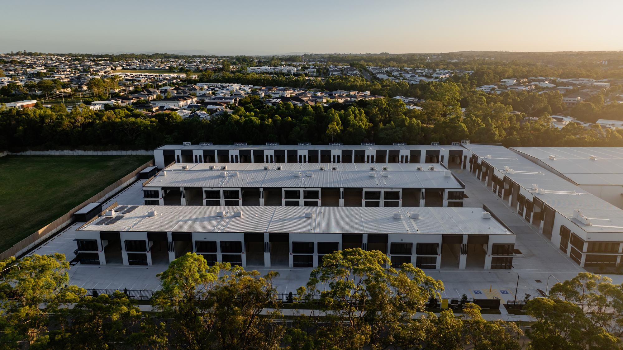 Aerial view of the completed development in daylight, three rows of units set against bushland and suburbs